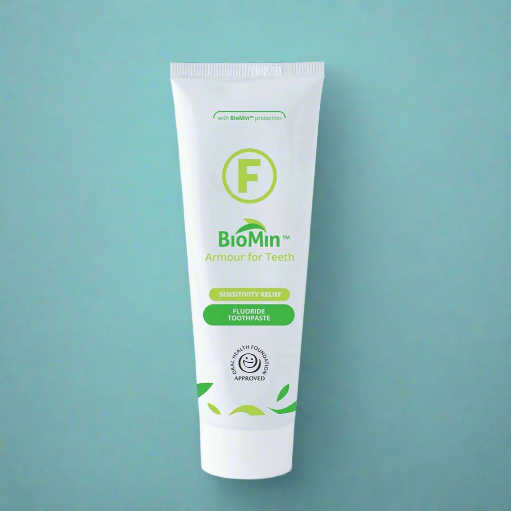 A white tube of BioMin F toothpaste labeled "Armour for Teeth" with fluoride protection. The tube features green leaf designs and a prominent green "F" symbol, over a light blue background, indicating fluoride content.