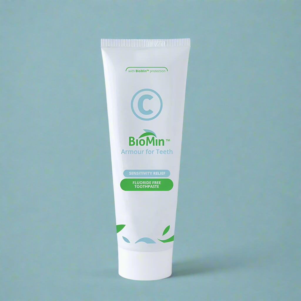 A white tube of BioMin C toothpaste labeled "Armour for Teeth" with fluoride free protection. The tube features green leaf designs and a prominent blue "C" symbol, over a light blue background, indicating fluoride free content.