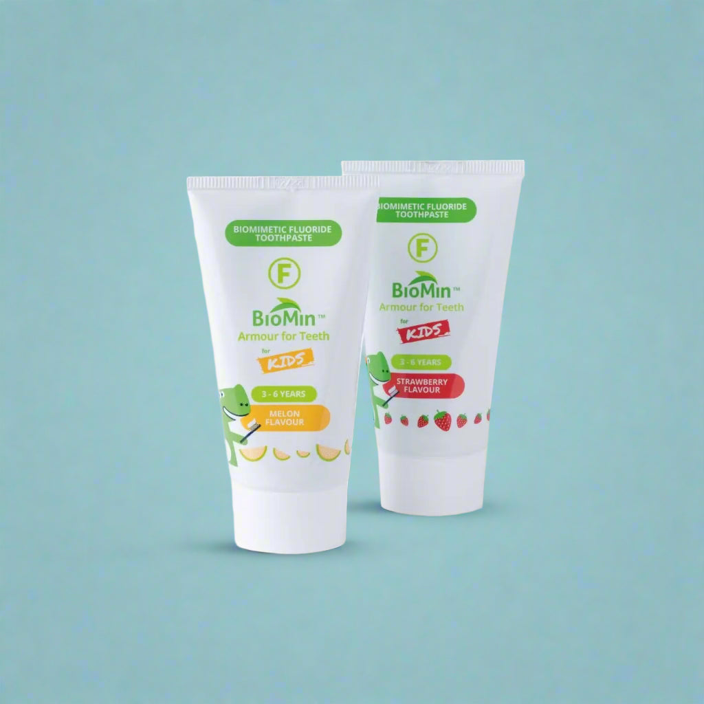 Two tubes of BioMin Kids toothpaste for children aged 3 to 6 years. One tube is melon-flavored, with a green dinosaur and melon slice graphics, while the other is strawberry-flavored, featuring strawberry illustrations. Both tubes are labeled with "Armour for Teeth" and "Biomimetic Fluoride Toothpaste", and over light blue background