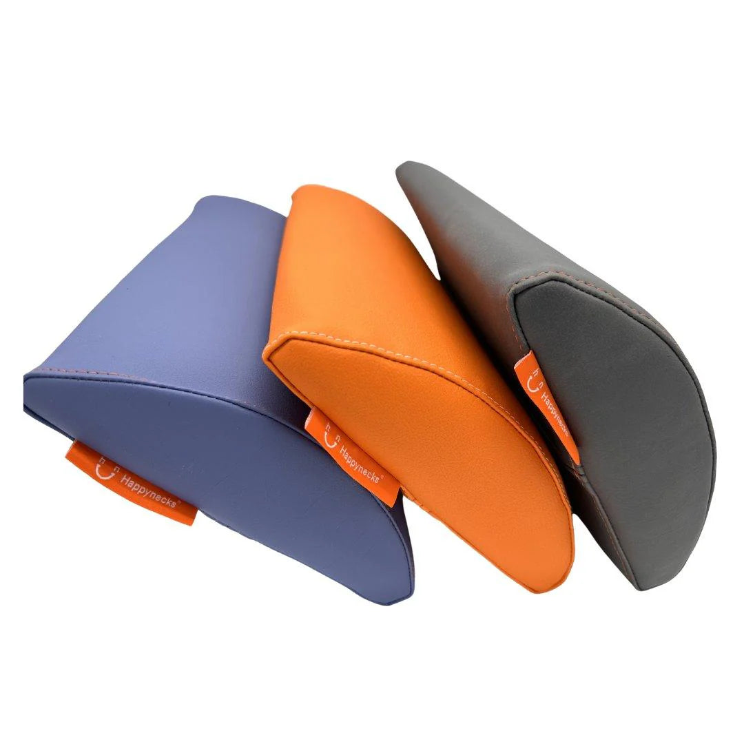 Three Happynecks® Pillows in different colors—blue, orange, and gray—are displayed side by side. Each pillow features an ergonomic design and an orange Happynecks® logo tag, showcasing their high-quality, durable construction for providing optimal support during dental or medical procedures. The background is white, highlighting the pillows' sleek design.