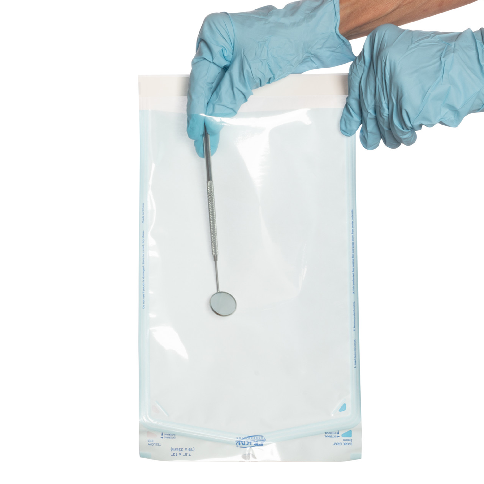 A pair of gloved hands is shown holding a transparent sterilization pouch containing a dental mirror. The pouch features a blue-tinted plastic window and a white self-sealing adhesive strip at the top, designed to maintain the sterility of medical or dental instruments. The background is white.