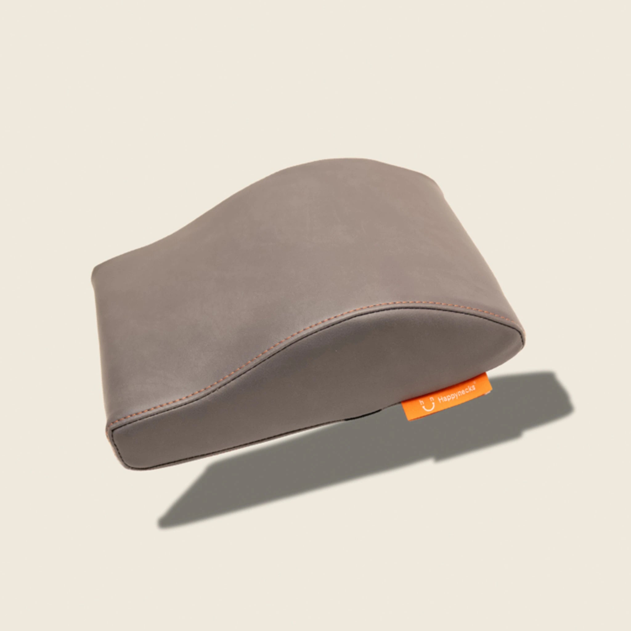 A contoured anthracite-colored support cushion designed for ergonomic comfort, featuring orange stitching and a small orange brand tag. Over white background.